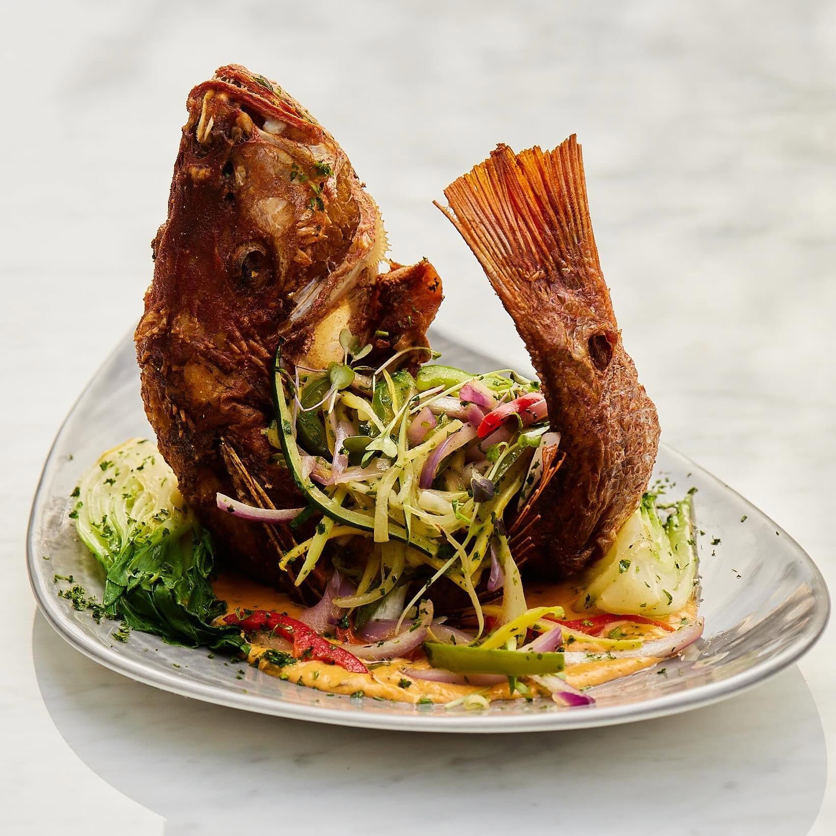 Two fried fish on a plate with shredded vegetables and sauce, garnished with lime wedges