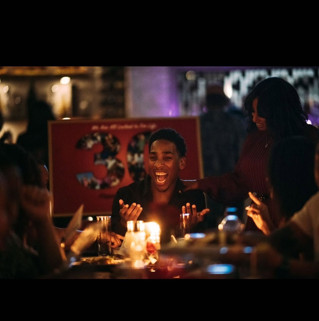 Candlelit dinner table with friends celebrating and laughing in a dimly lit restaurant or bar.