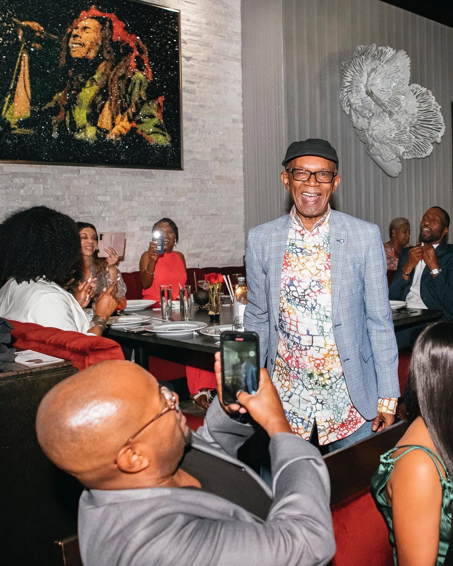 Smiling man in blue blazer at a lively restaurant table with seated guests and wall art nearby