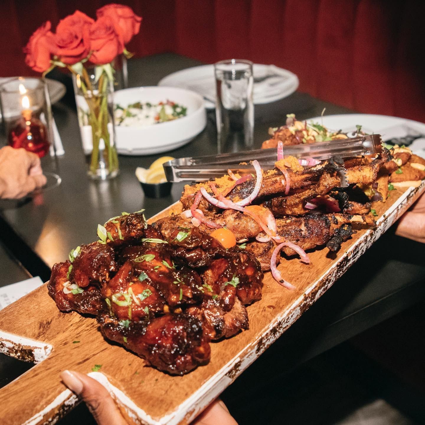 Platter of glazed ribs topped with onions on a dining table with roses and plates in the background