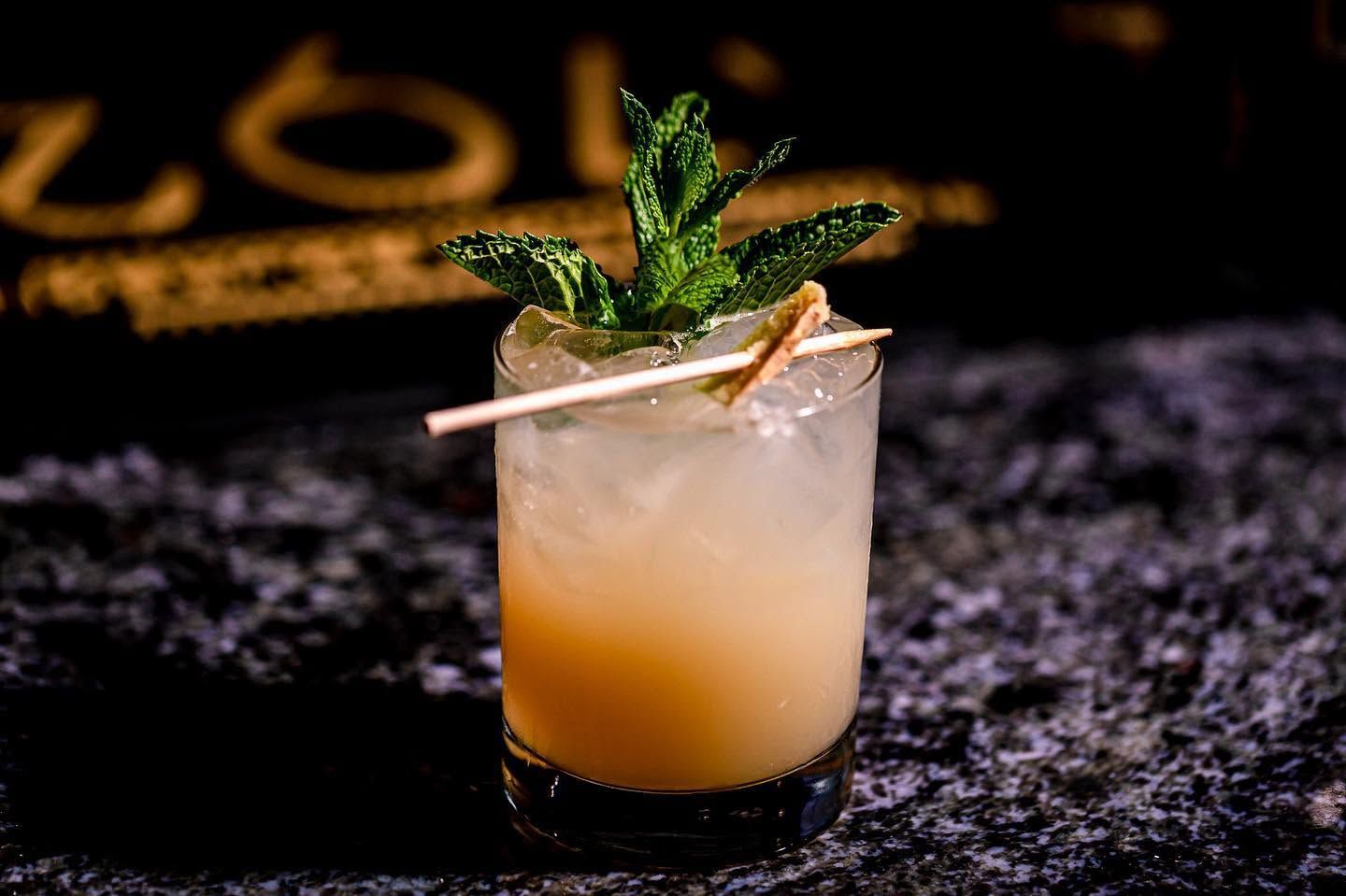 Mint garnish on a frothy citrus cocktail in a short glass on a dark bar surface.