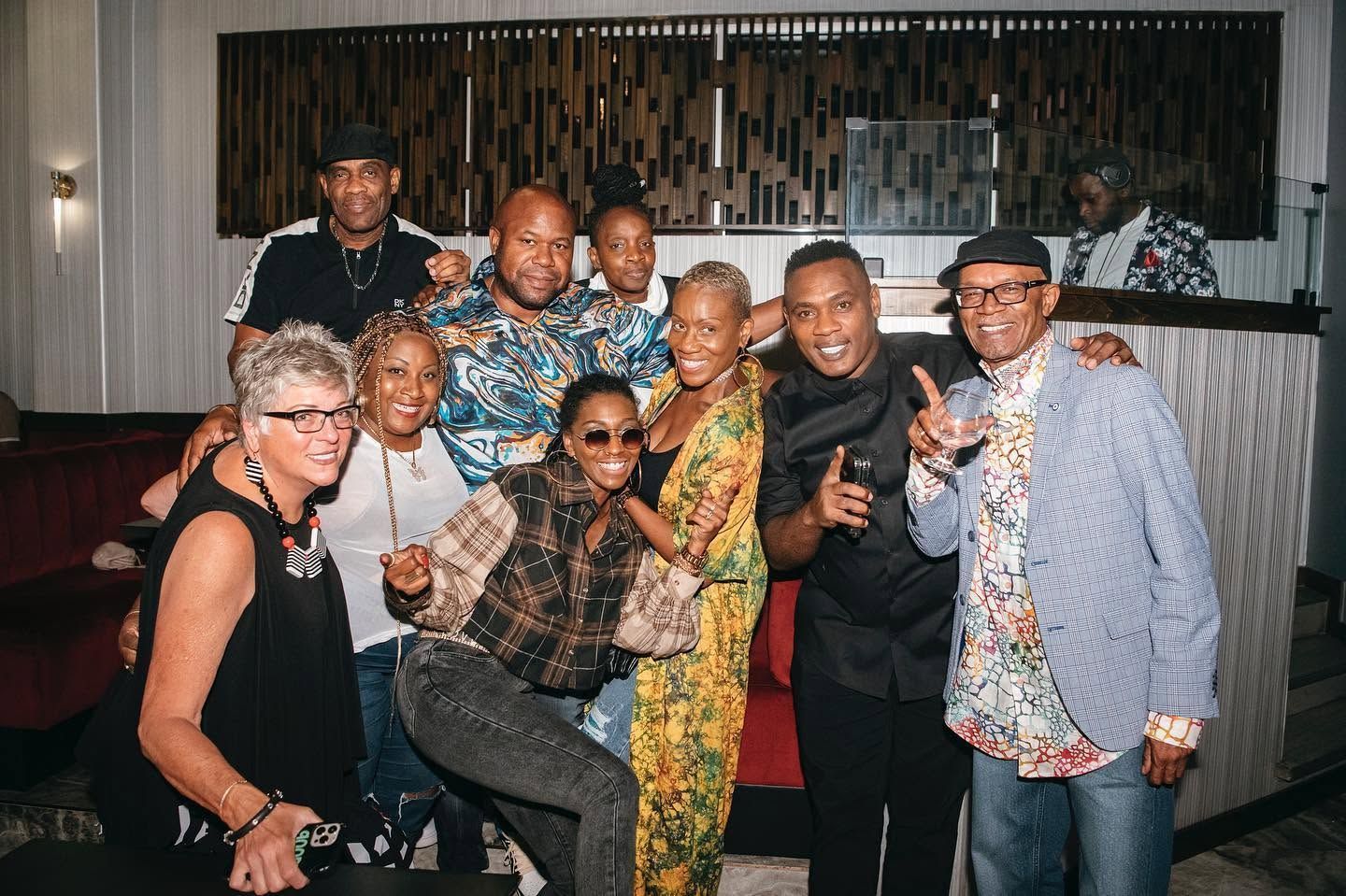 Group of smiling people posing together indoors at a party, dressed in colorful casual outfits.