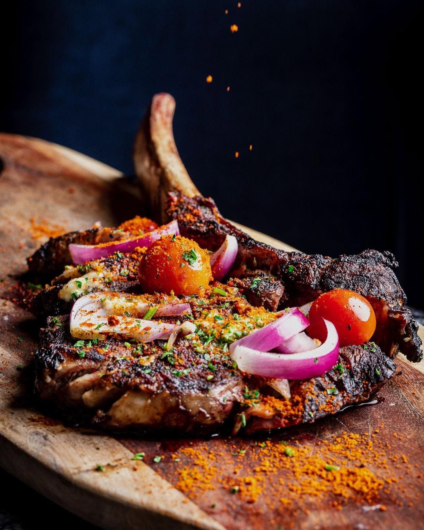 Grilled meat dish topped with onions, peppers, and spices on a wooden board