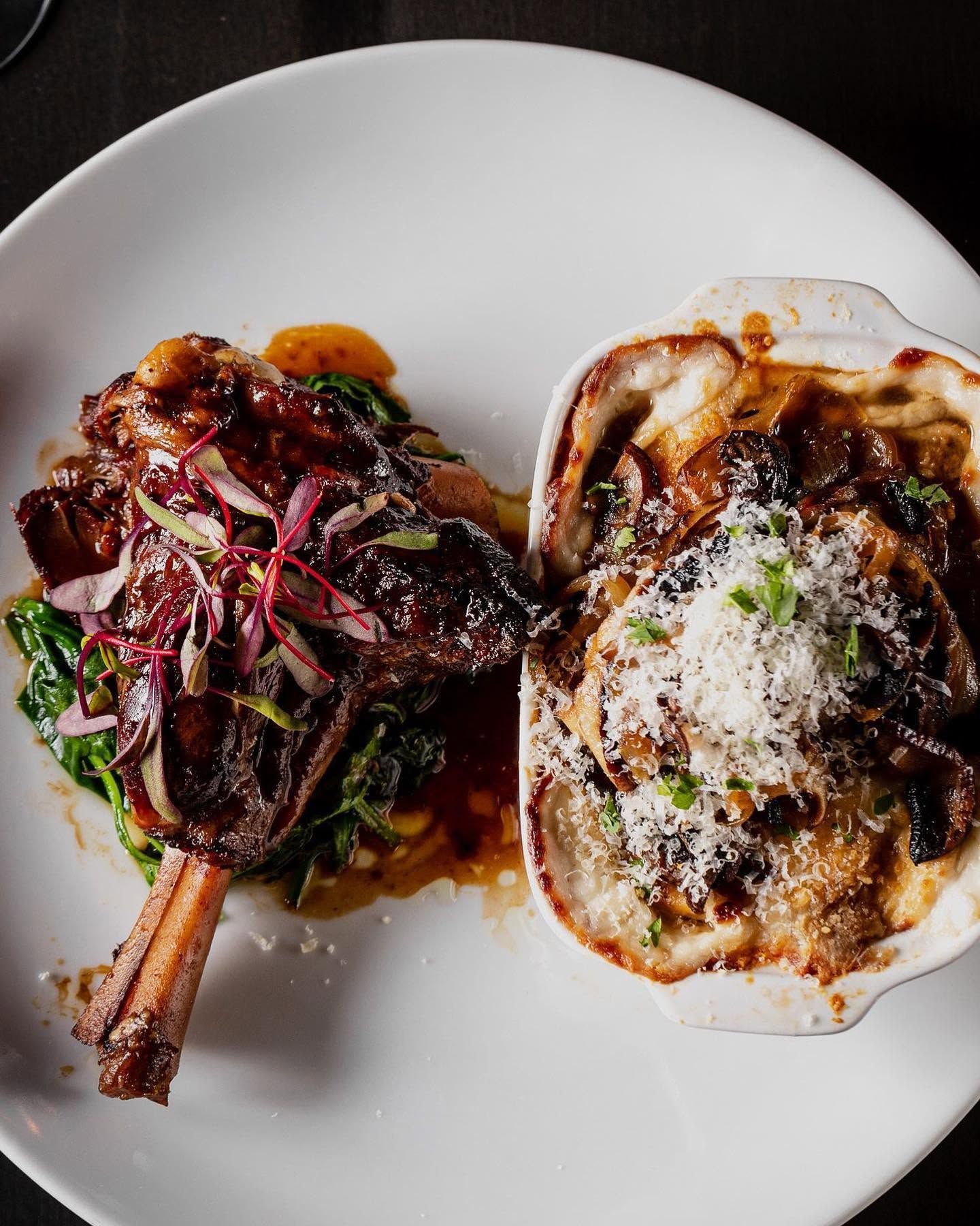 Plated gourmet dish with saucy meat and a toasted bread slice, topped with melted cheese and herbs.