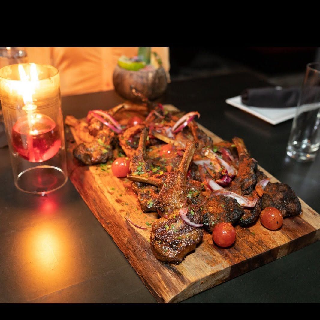Grilled meat skewers on a wooden board with cherry tomatoes and candlelight on a dark table