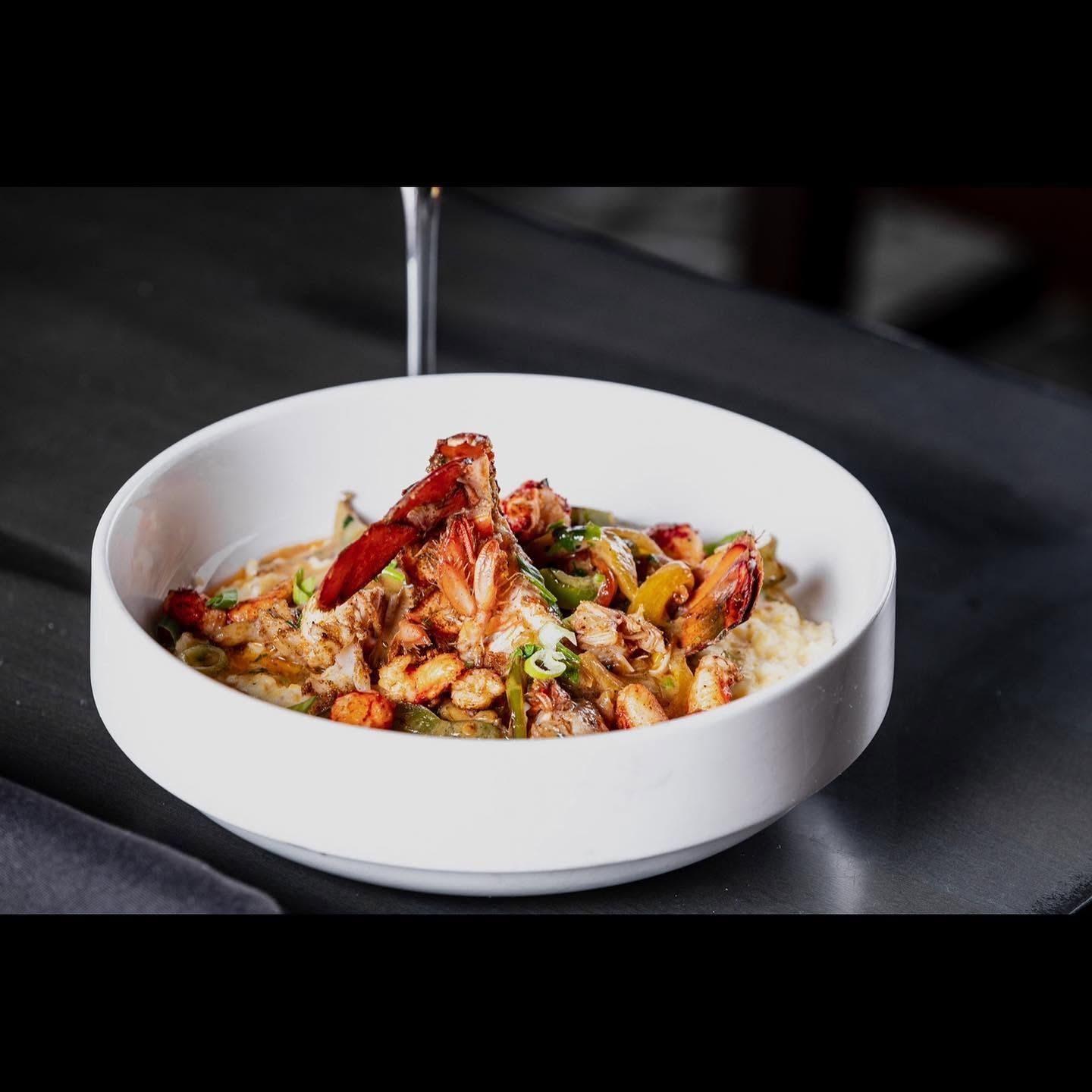 White bowl of pasta topped with bacon and herbs on a dark tabletop