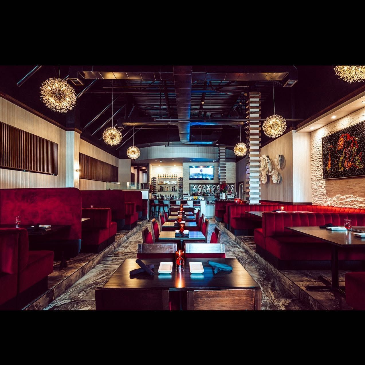 Stylish restaurant interior with red booth seating, hanging lights, and a central aisle to the bar