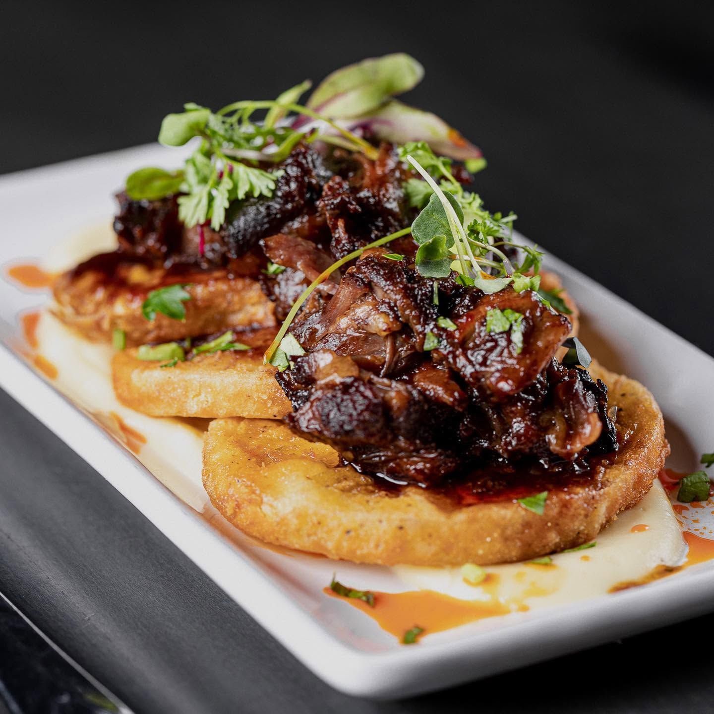 Plated gourmet appetizer with seared meat, herbs, and toasted bread on a white rectangular dish