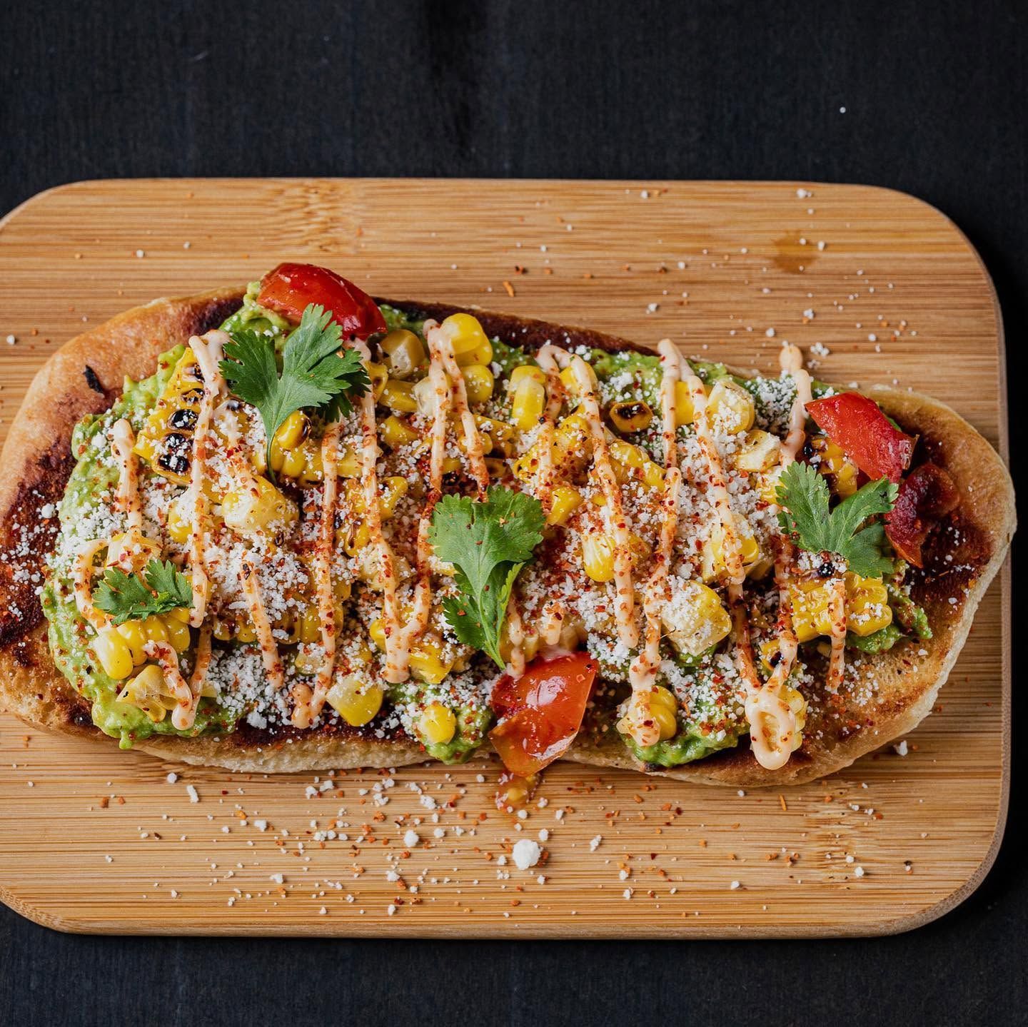 Grilled open-faced sandwich topped with drizzled sauce, herbs, and strawberries on a wooden board