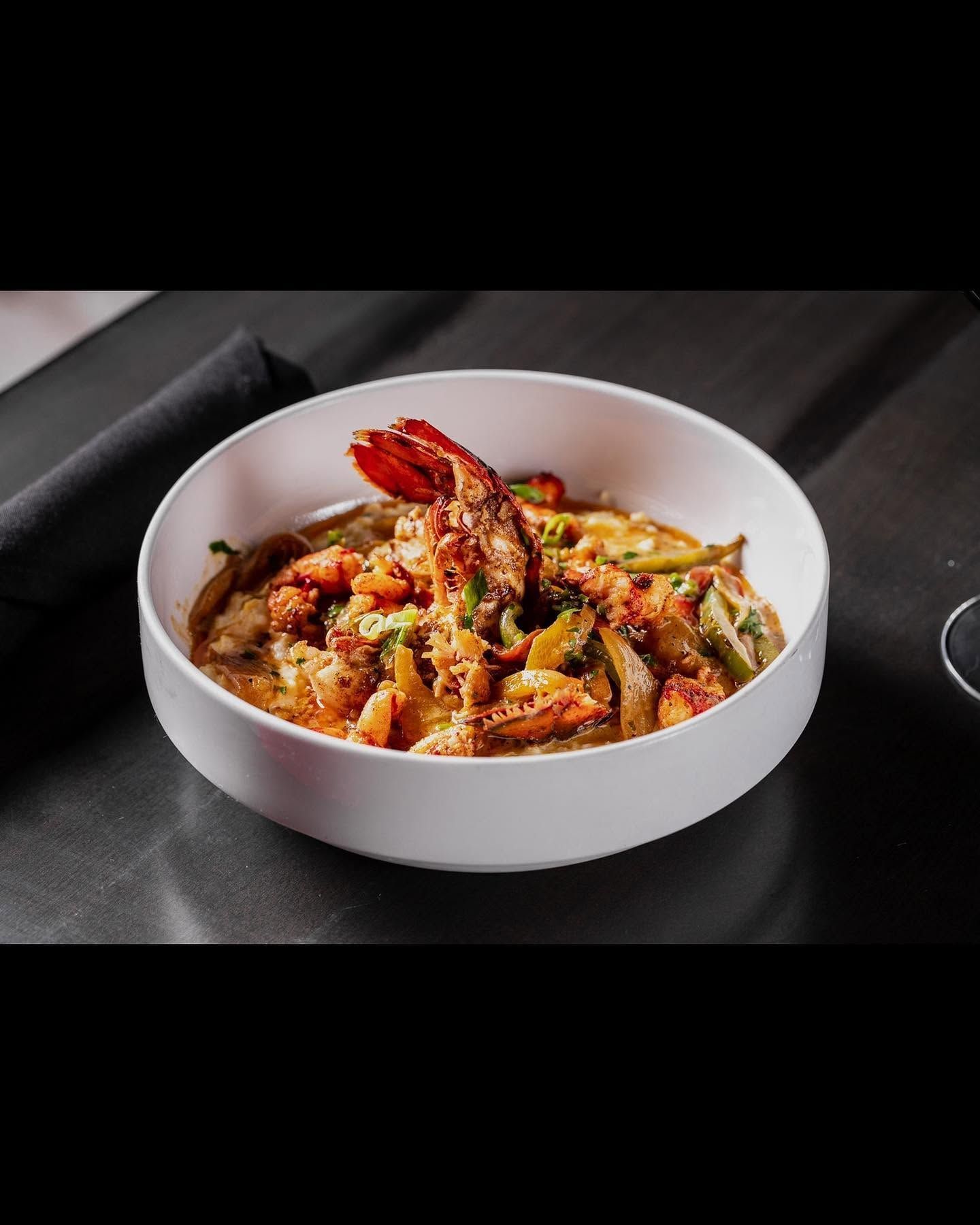 White bowl of spicy seafood pasta with shrimp and vegetables on a dark table