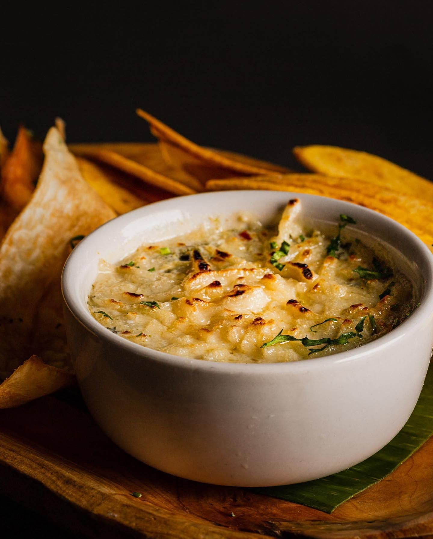 Bowl of creamy dip topped with herbs, served with tortilla chips on a wooden board