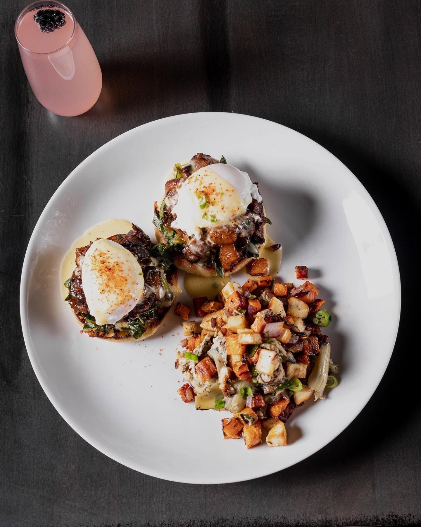 Plated breakfast of eggs, avocado toast, and diced potatoes beside a pink drink on a dark table