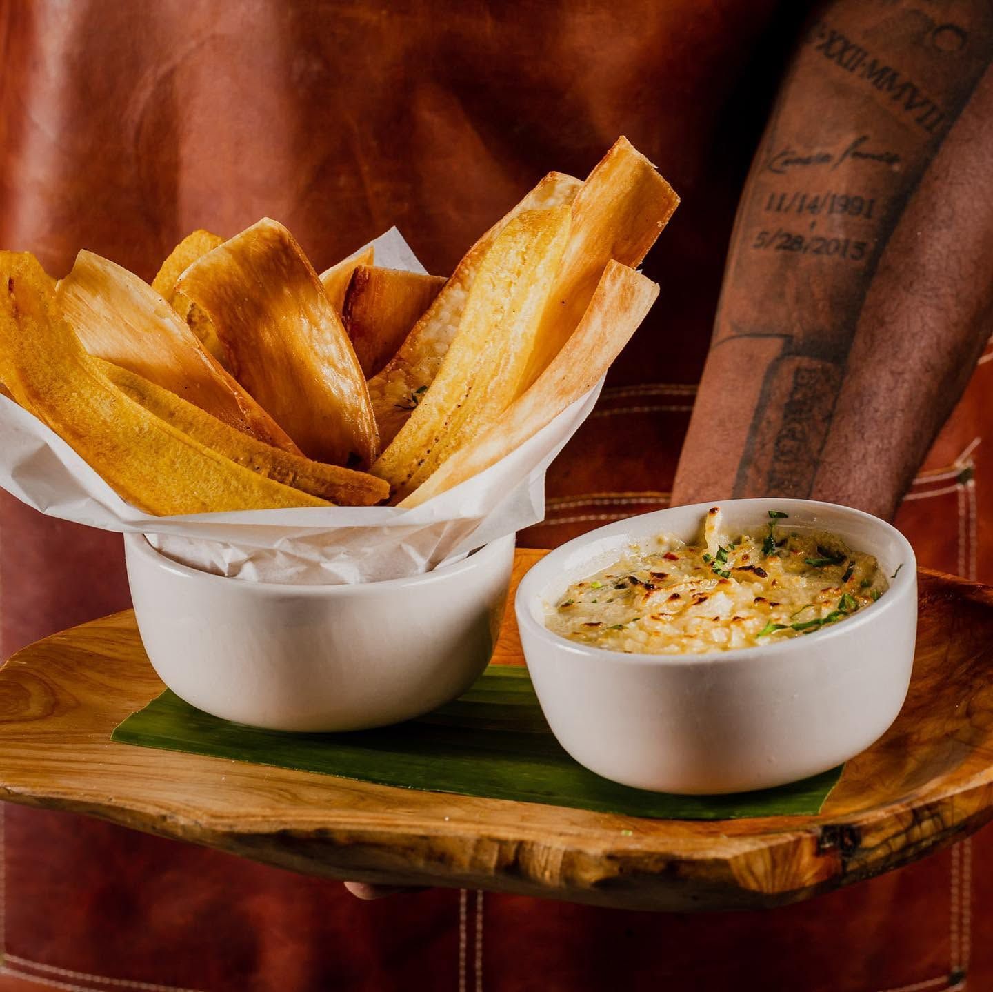 Golden fried breadsticks in a bowl with a creamy dipping sauce on a wooden board