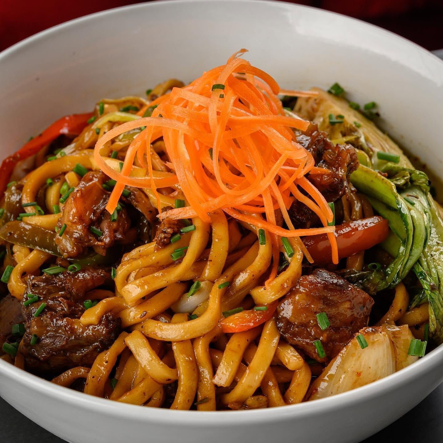 Bowl of noodles with beef, vegetables, and shredded carrots topped in the center