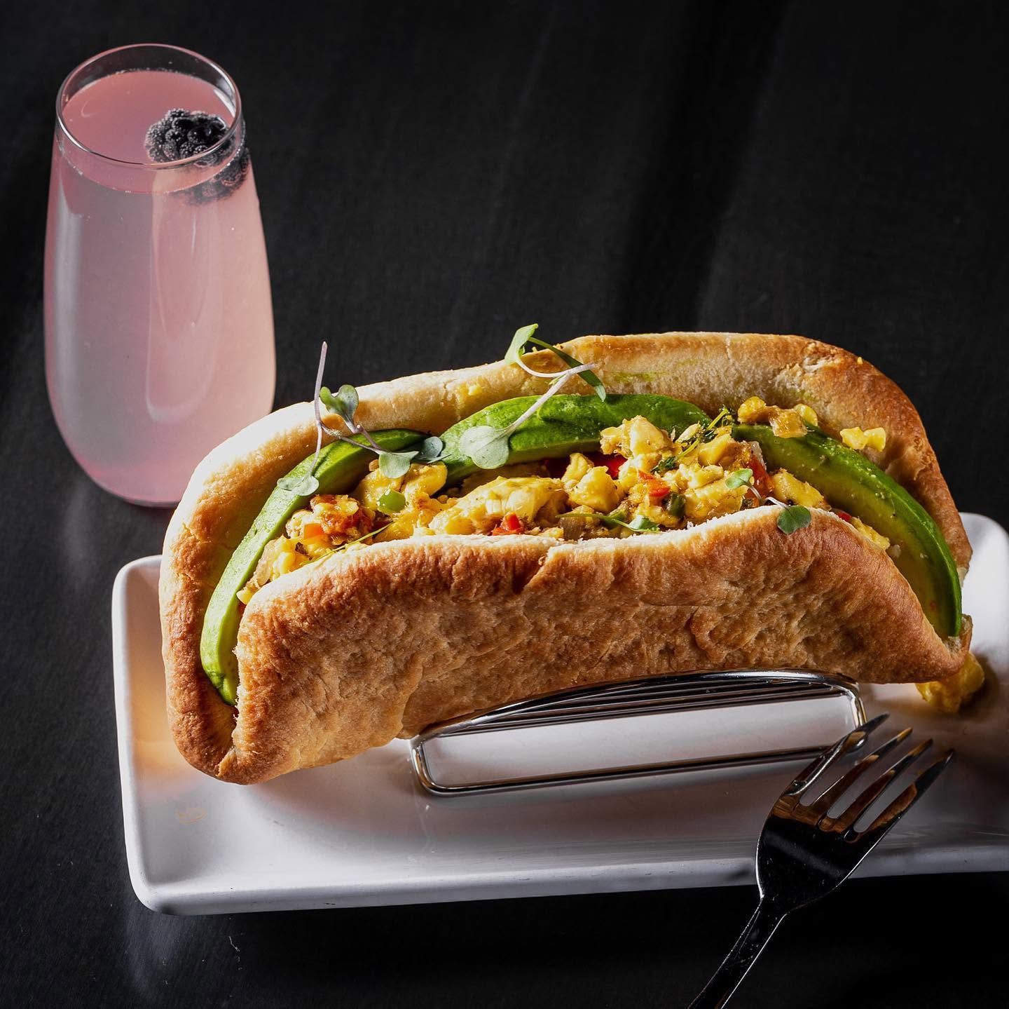 Open-faced sandwich on white plate with pink drink, dark background