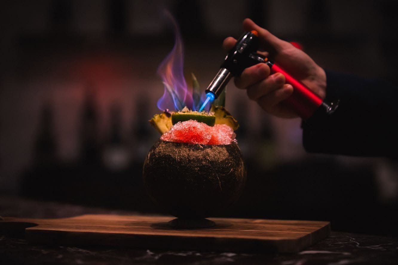 Hand torch caramelizing a colorful dessert on a wooden board, with blue and purple flames
