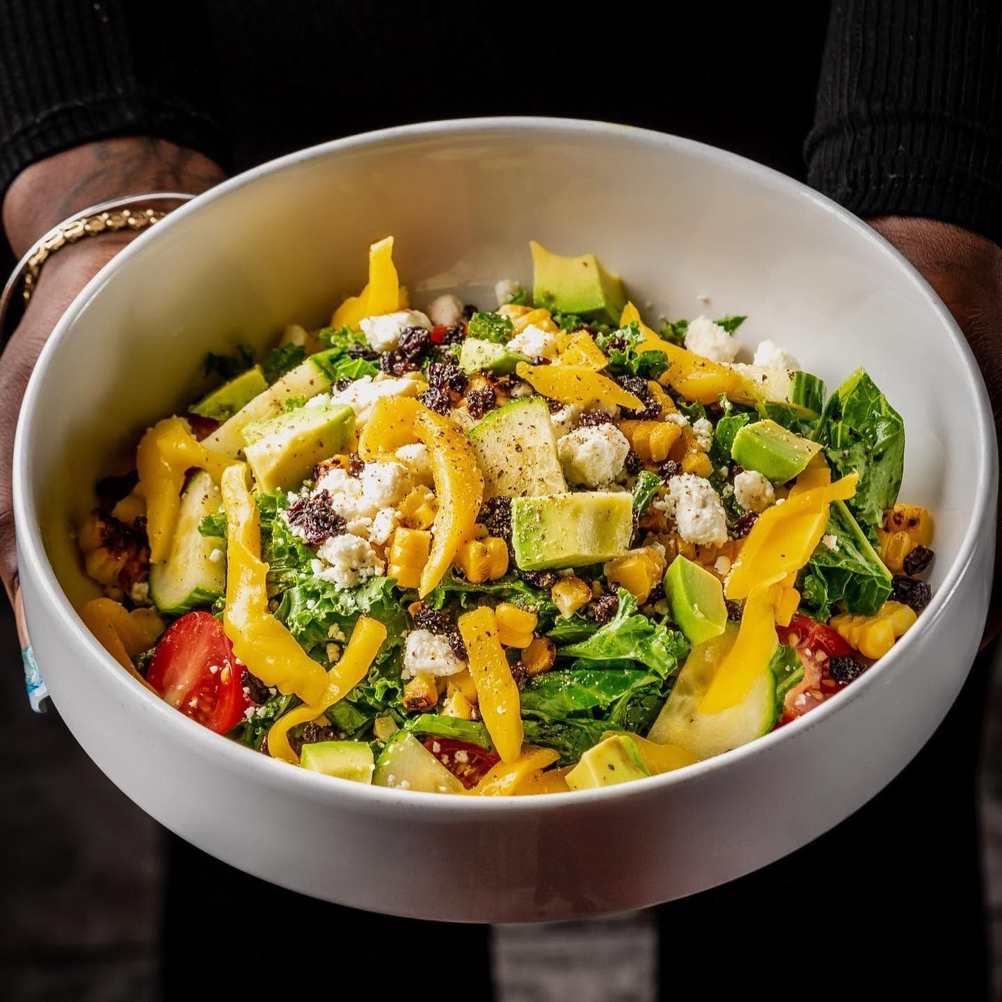 Bowl of colorful chopped salad with greens, mango, avocado, strawberries, and seeds