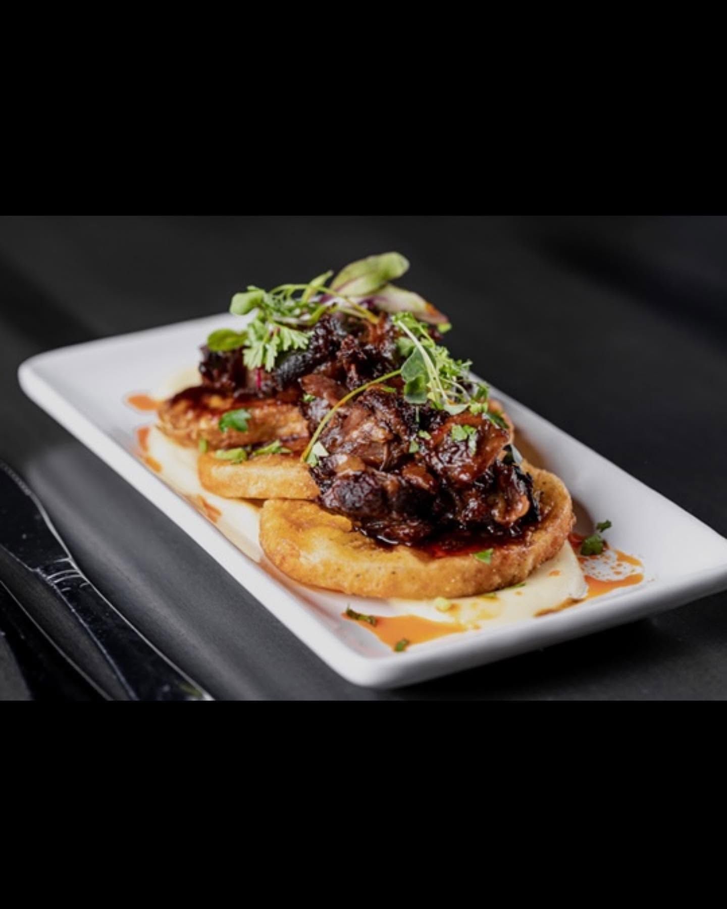 Gourmet dish of seared meat on toasted bread with sauce and microgreens on a white plate