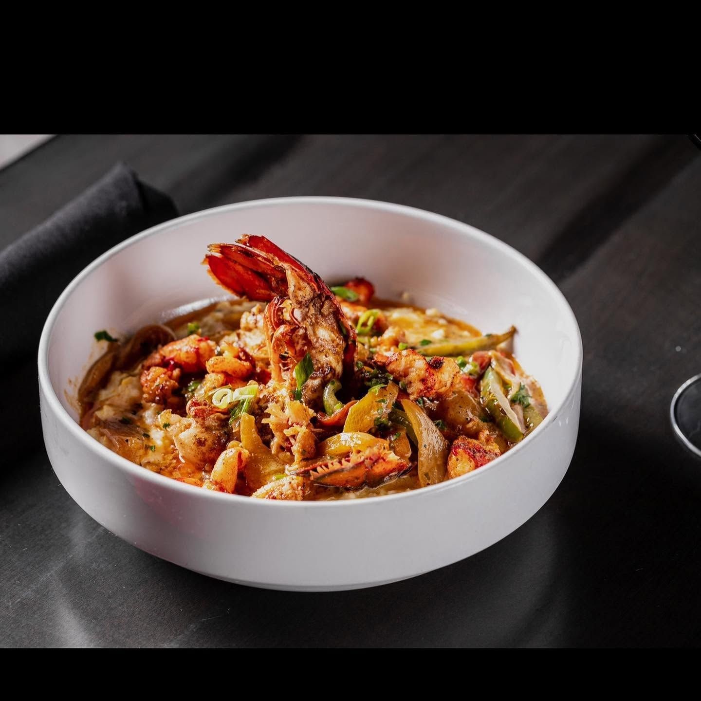 White bowl of spicy sauced shrimp and vegetables on a dark table