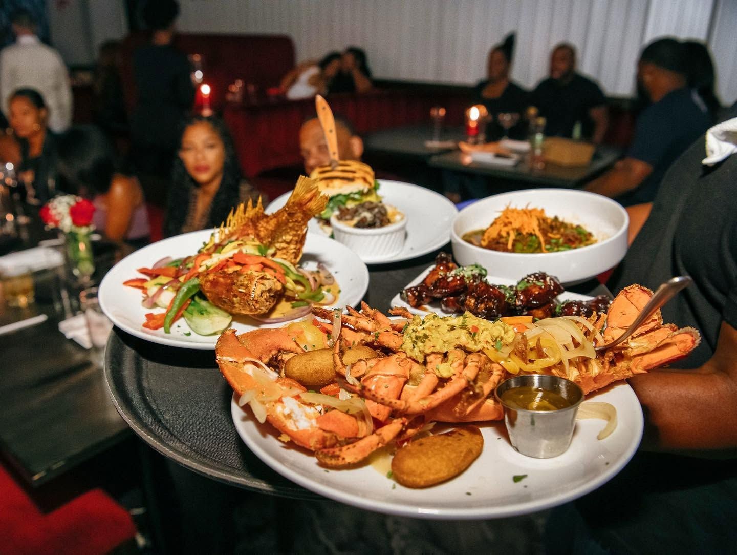 Plated seafood dishes on a restaurant table, with dimly lit diners in the background