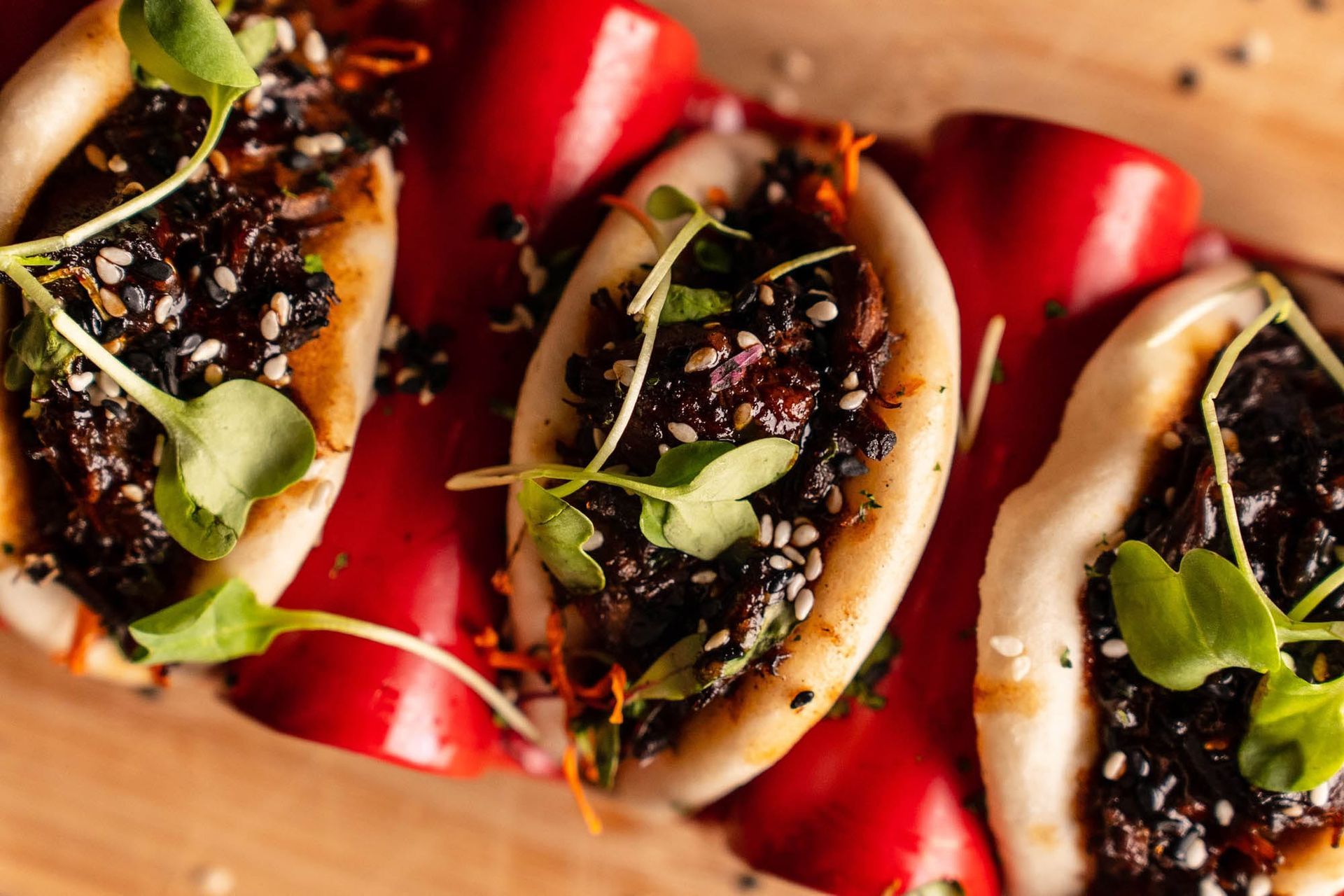Three tacos with black bean filling and cream on a wooden board, garnished with greens and red peppers
