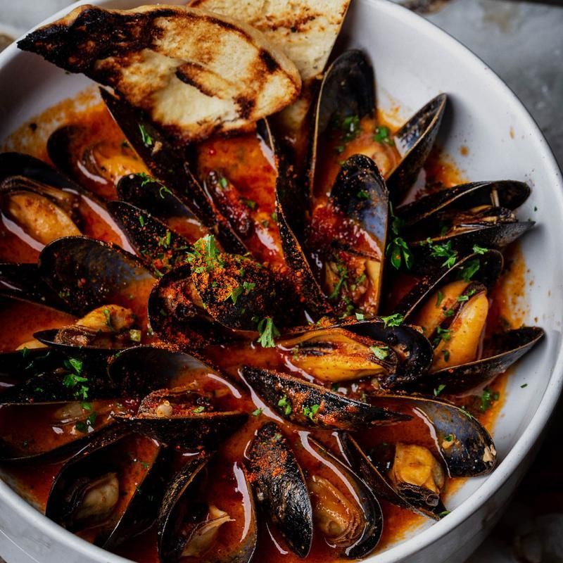 Plate of mussels in red sauce with grilled bread slices and herbs