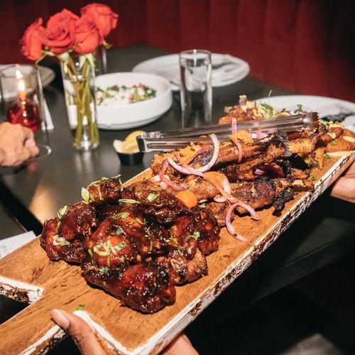 Tray of glazed grilled meat skewers topped with onions on a dining table with flowers and plates
