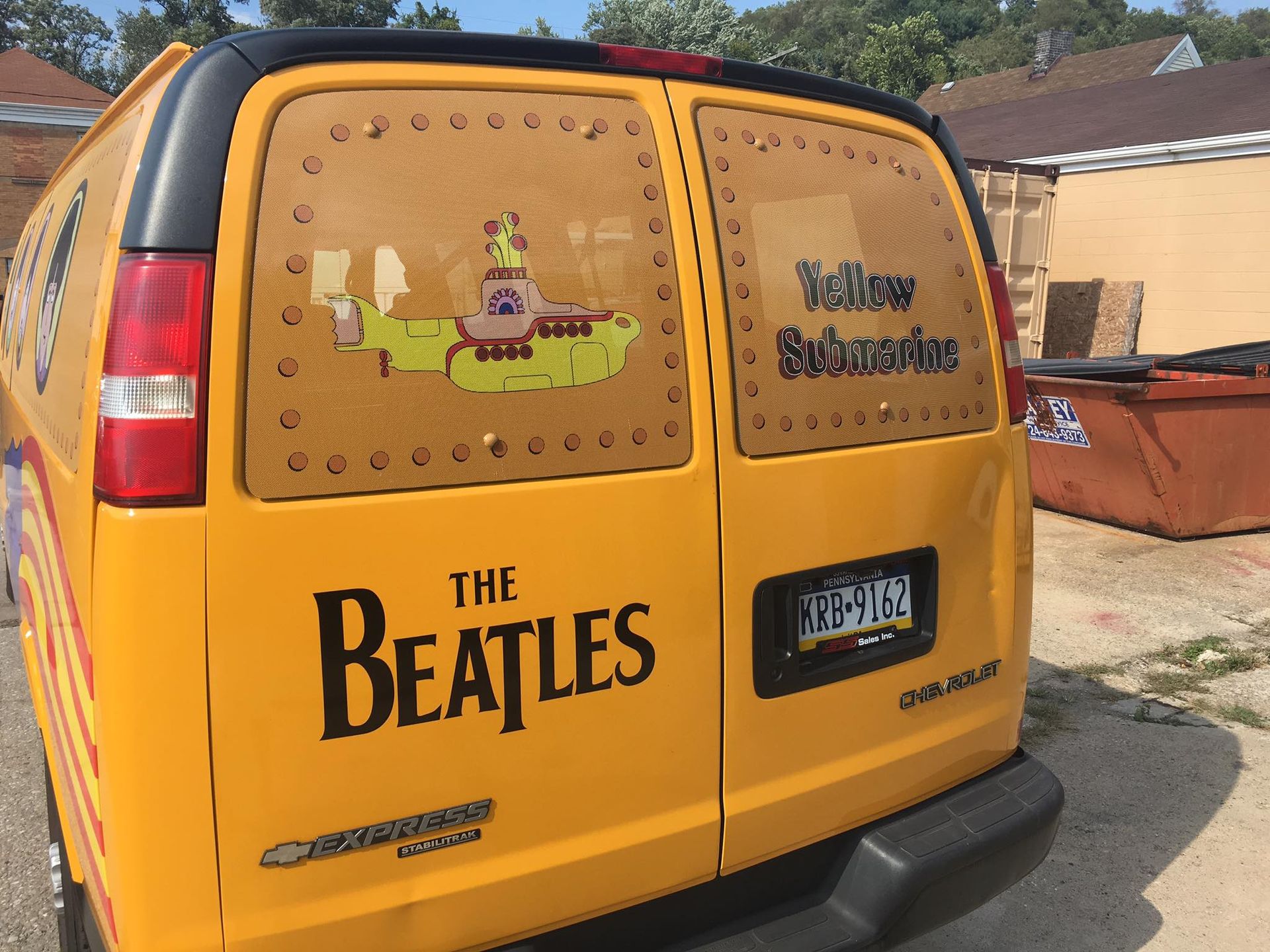 A yellow van with the beatles on the side is parked on the side of the road