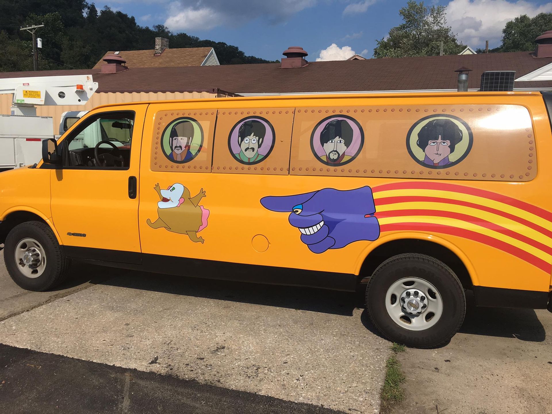 A yellow van with the beatles on the side is parked on the side of the road