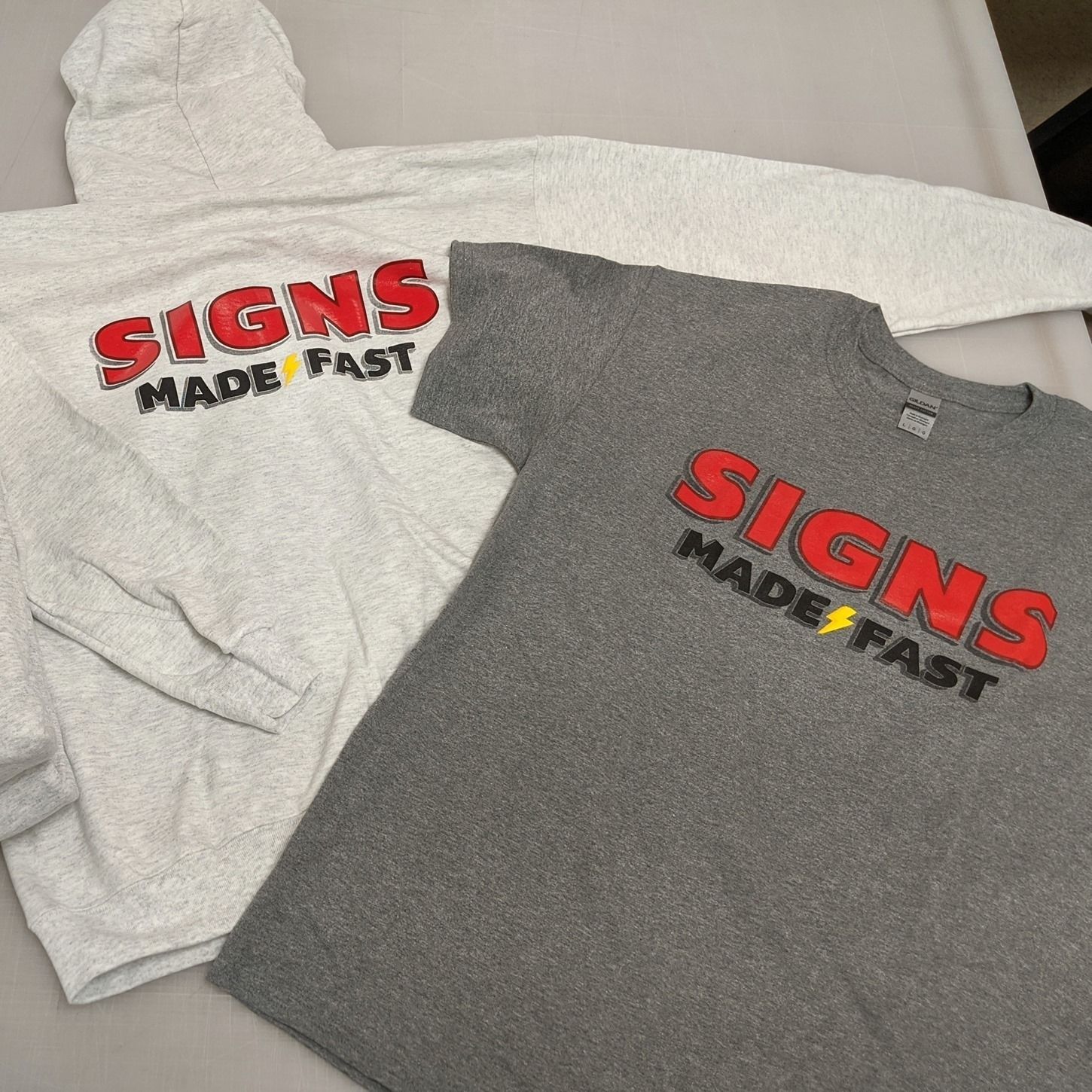 A hoodie and a t-shirt with the words `` signs made fast '' embroidered on them are sitting on a table.