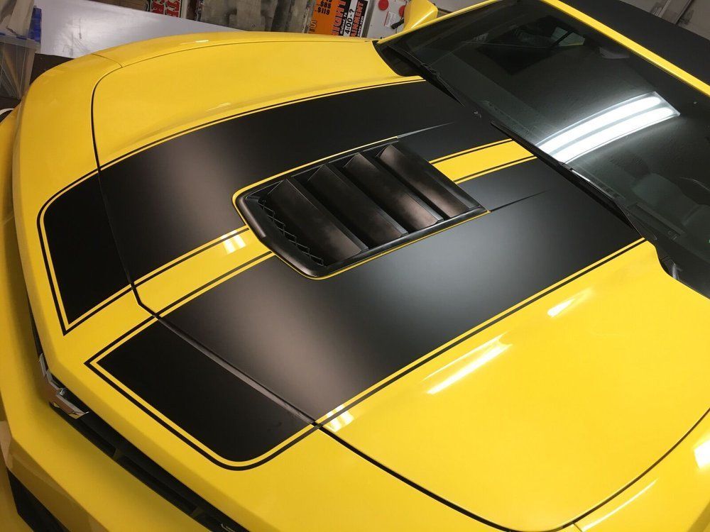 A yellow car with black stripes on the hood