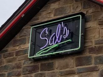 A neon sign on a brick wall says Sal's