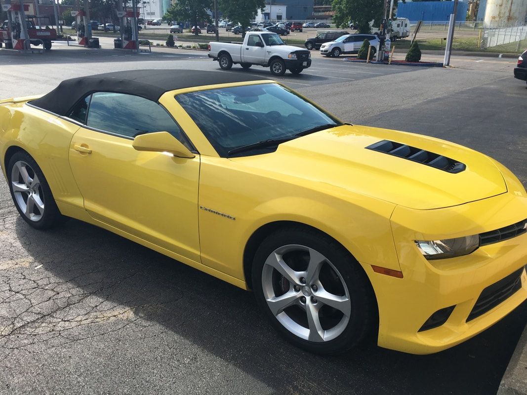 A yellow convertible car is parked on the side of the road.