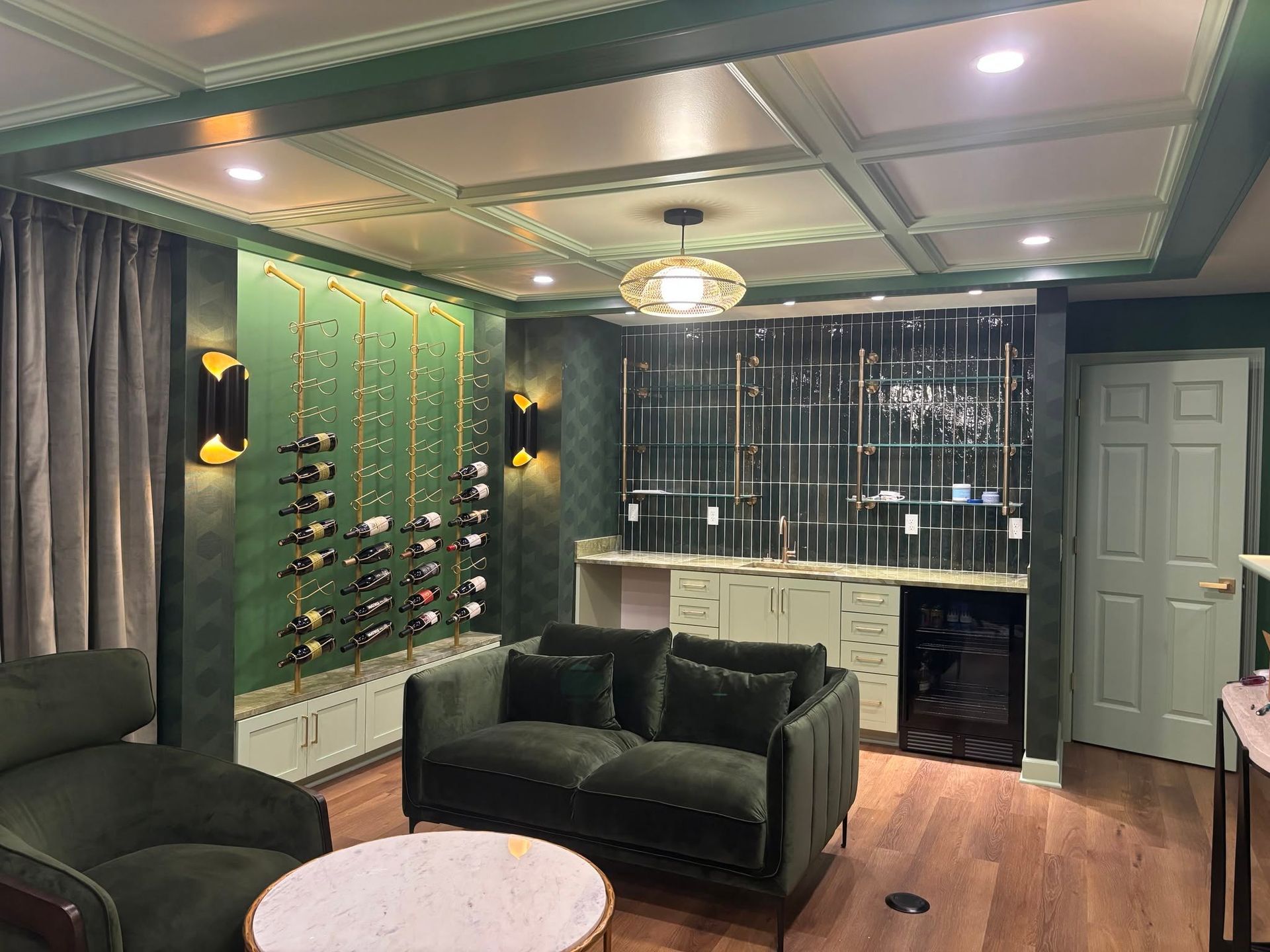 Stylish lounge with green velvet sofas, marble table, bar sink, and metallic wall decor