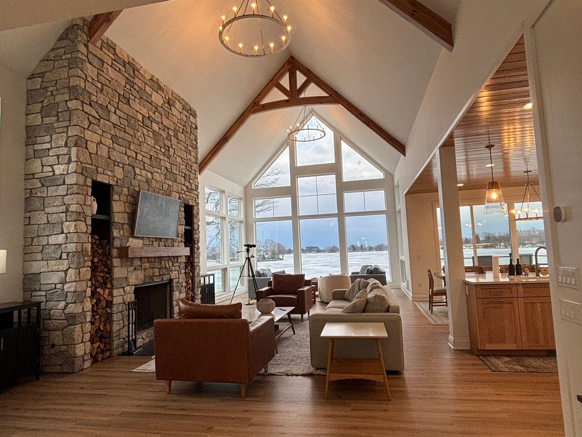 Cozy lodge living room with stone fireplace, vaulted wood beams, and large windows overlooking water