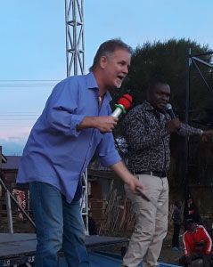 A confident man on a stage, holding a microphone.