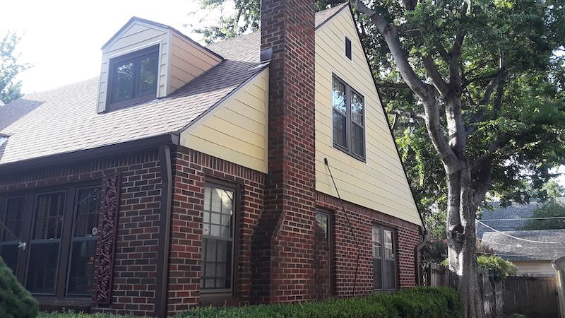 A brick house with a yellow siding and a chimney