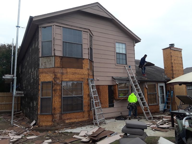 A man is standing on the roof of a house with a ladder.