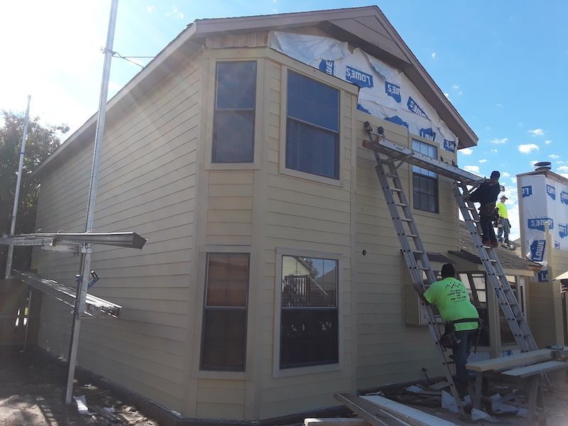 A man on a ladder is painting the side of a house