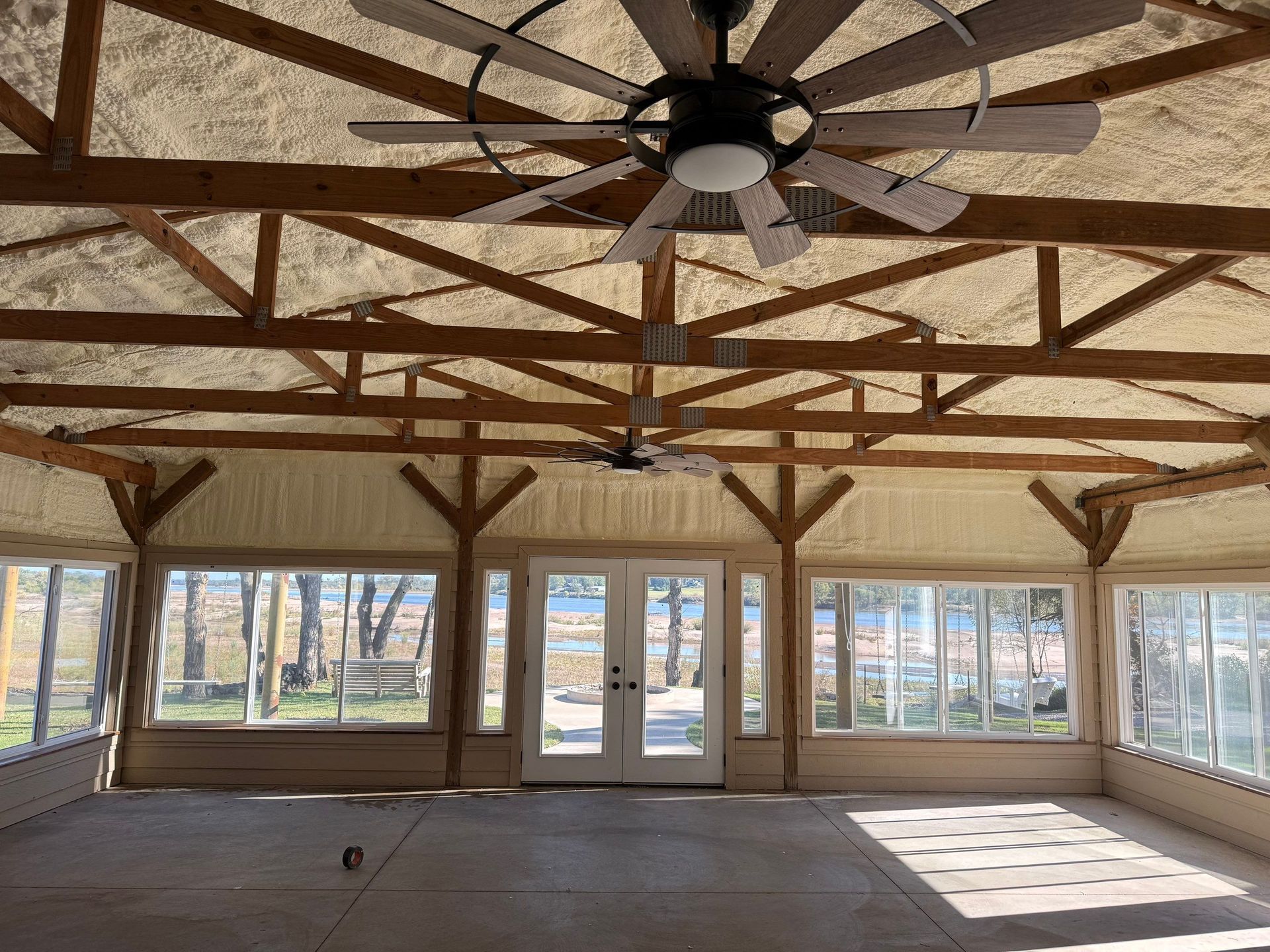 Interior view of a sunroom with exposed wooden beams, two ceiling fans, and large windows with a view.
