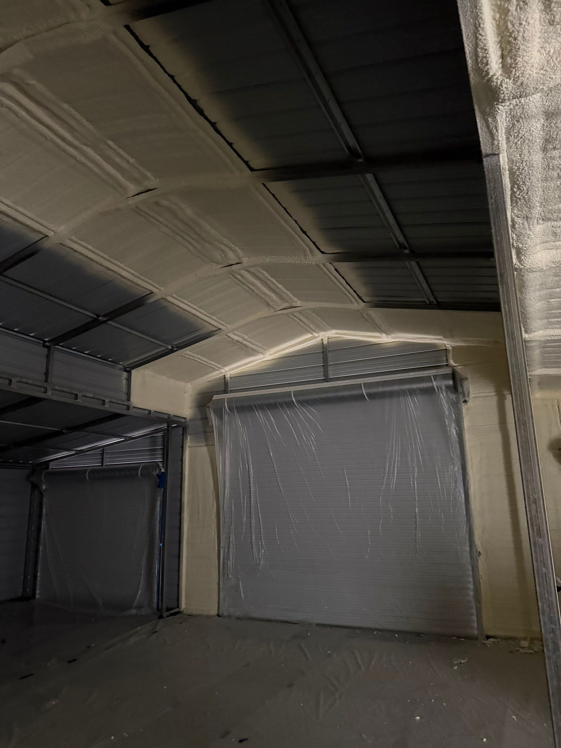 Inside of a warehouse, overhead doors are closed.  Dust or debris coats the ceiling and upper walls.