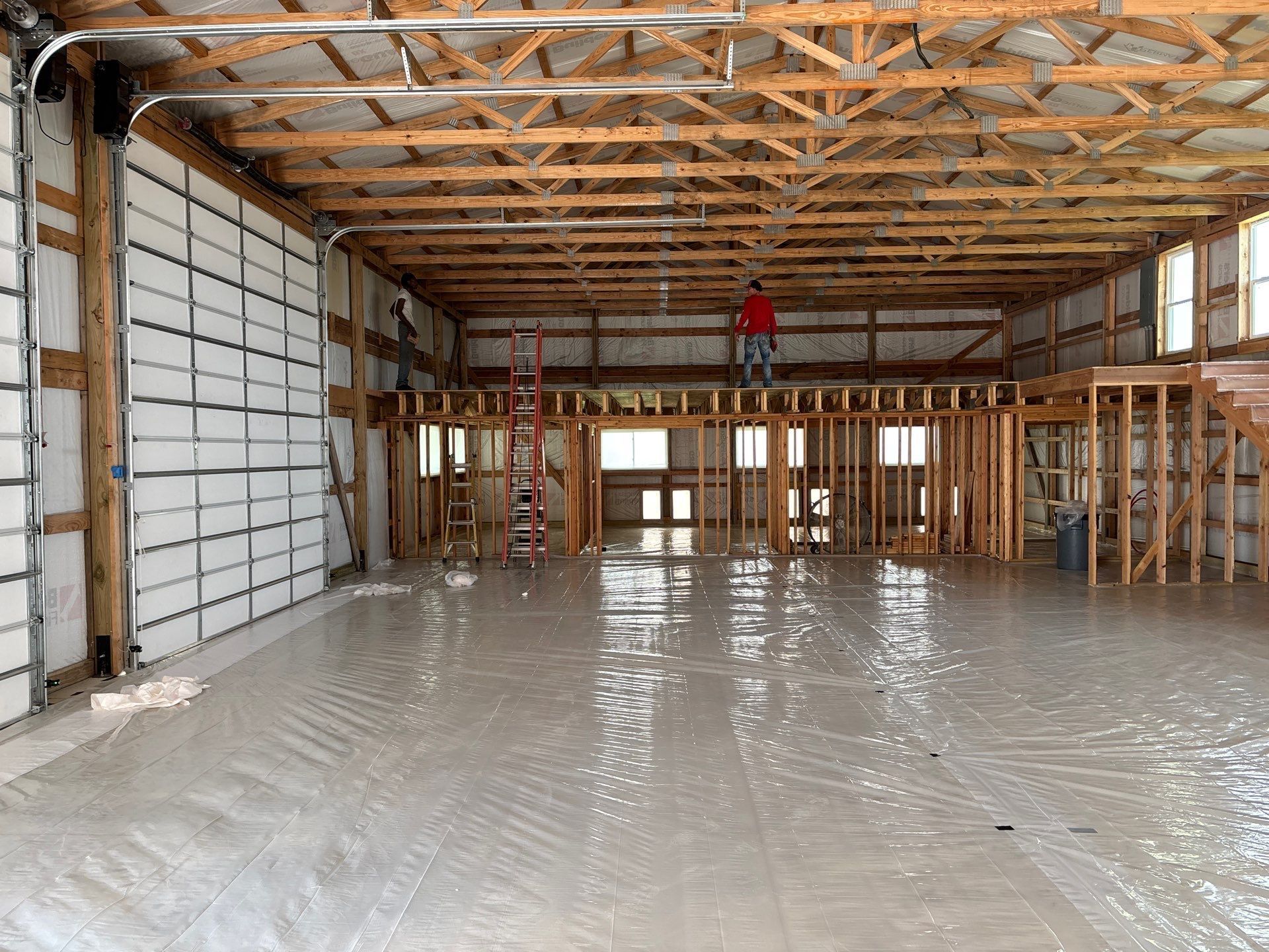 Interior view of a large unfinished building with a concrete floor. A person stands on a wooden platform.