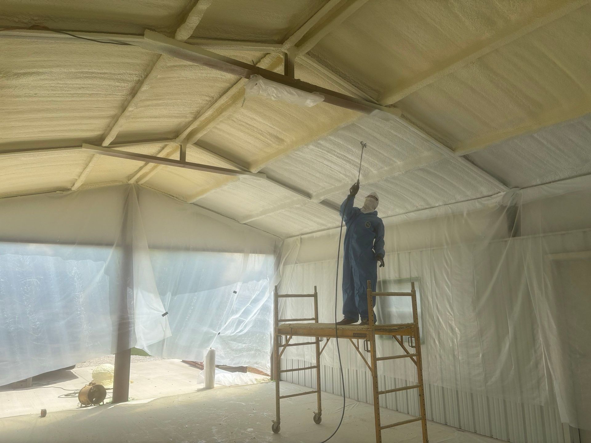 Man in protective suit spraying insulation foam inside a building with a scaffolding.