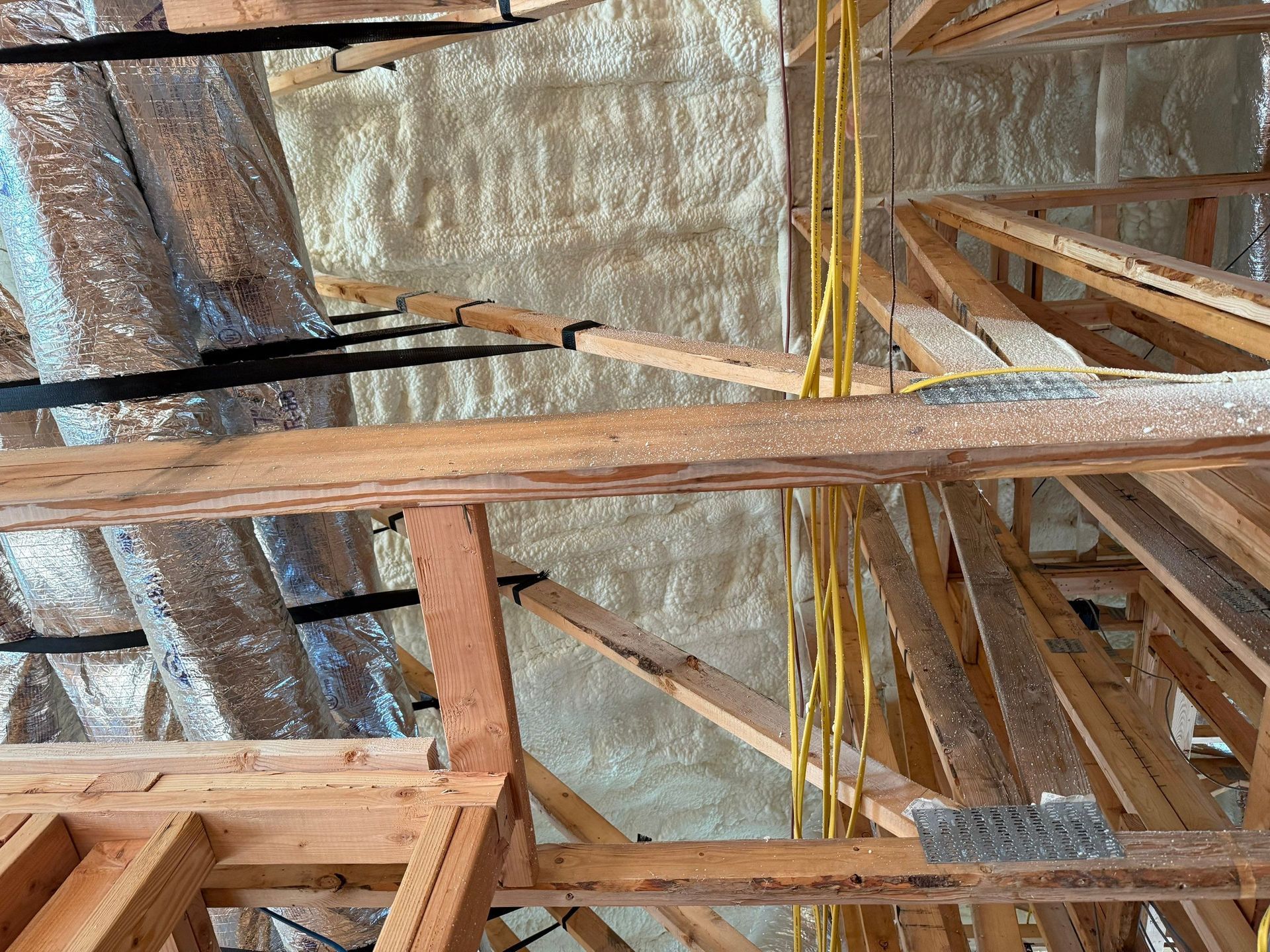 Attic rafters and insulation: Wood beams, spray foam insulation, and electrical wiring.