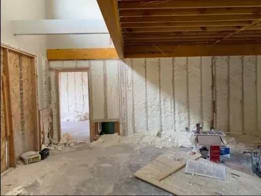 Room under construction with spray foam insulation on walls, exposed beams, and open doorway.