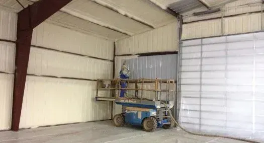 Man on a lift applying insulation to the interior walls of a metal building.