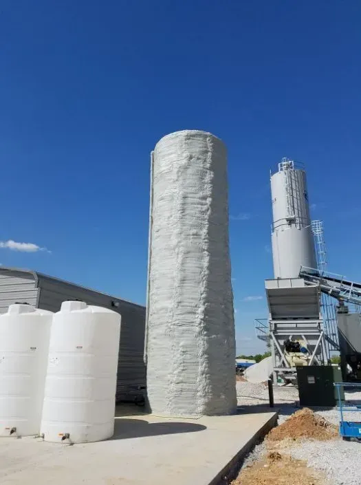 Large, cylindrical silo wrapped in white material, adjacent to other industrial structures and storage tanks.