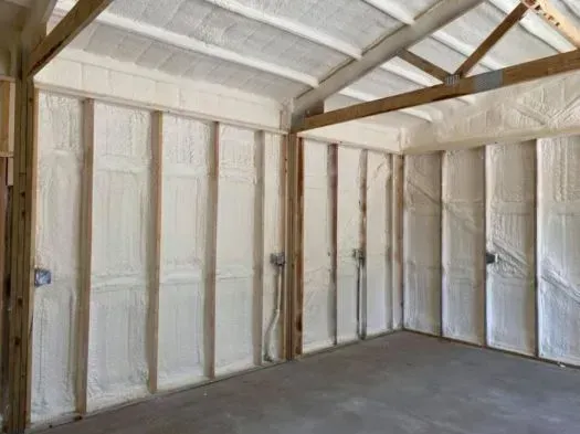 Interior of a room with exposed wooden studs filled with white spray foam insulation; concrete floor.