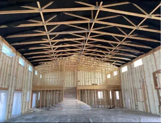 Interior view of a building under construction, showing wooden trusses and framed walls.