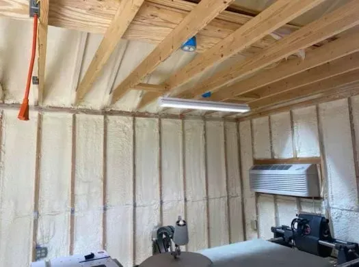 Interior of a building with spray foam insulation on walls and ceiling, exposed wooden beams, and a light fixture.
